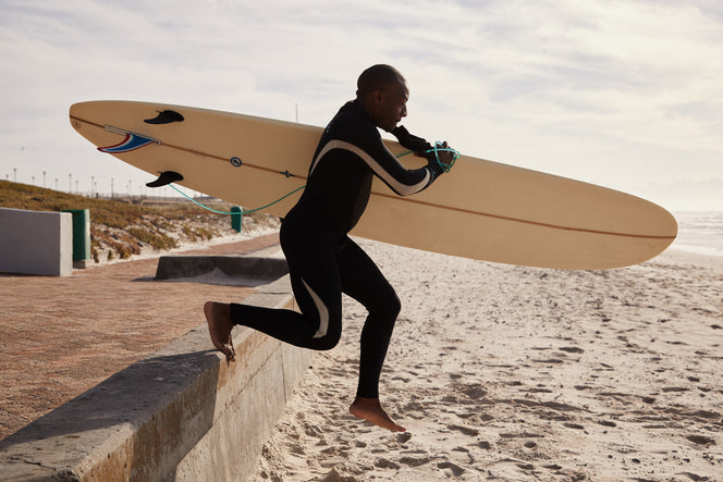 man with surfboard sprinting on the sand